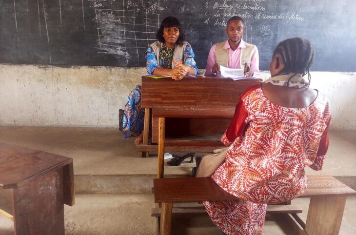 Sur les bancs d'une école, une femme est vue de dos, face à deux personnes (assises à la place du professeur) qui semblent l'écouter, lors de l'audition des victimes devant la Commission vérité du Kasaï en République démocratique du Congo (CVPJR).
