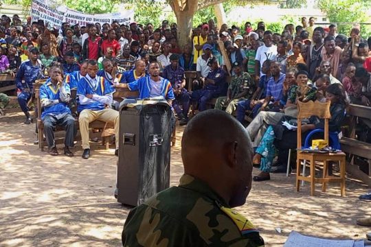 Audience foraine dans un village du Kasaï (RDC). Les 7 accusés du procès Kamuina Nsapu sont au centre, entourés de militaires et d'une foule de villageois.