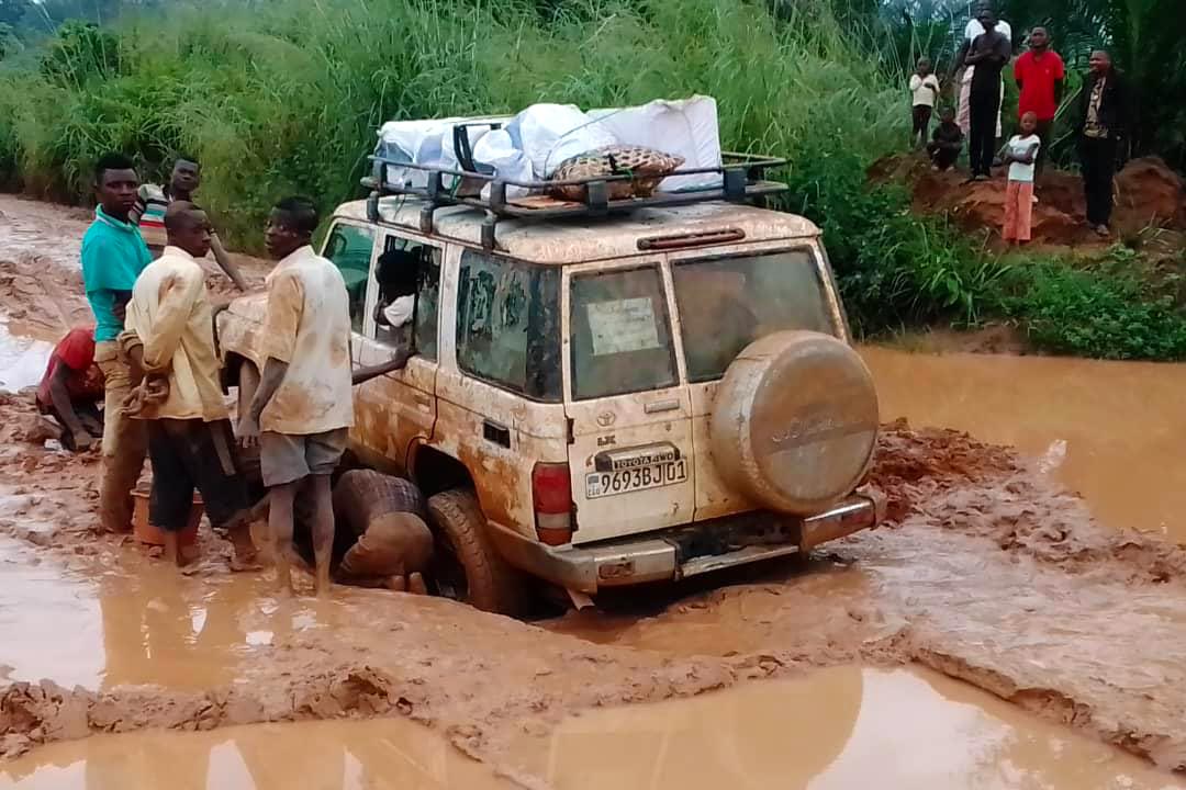 La voiture de notre correspondant est embourbée sur le chemin du procès, au Kasaï. Des habitants locaux aident le chauffeur.