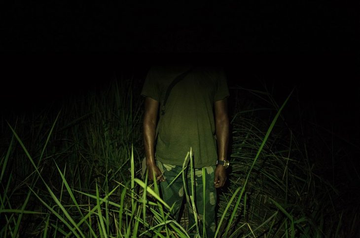 A man in military clothing stands outside (Yumbi area). His face is not visible.