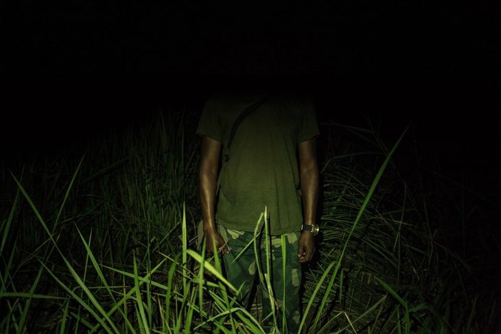 Un homme en habits militaires se tient debout en extérieur (région de Yumbi). Son visage n'est pas visible.