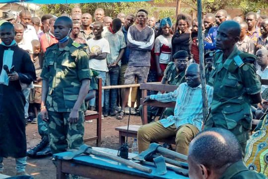 An outdoor trial with lawyers, military, civilians and the public standing around