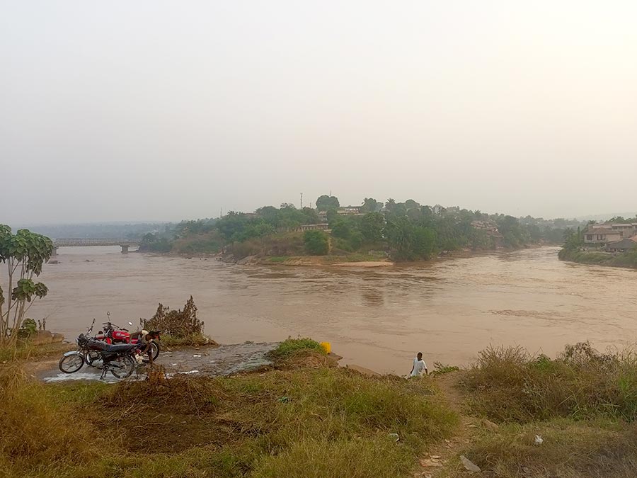 A wide shot shows the two rivers, the Kasai and the Tshikapa, converging below a vantage point where two motorbikes are parked side by side. A man is walking up from the river below.