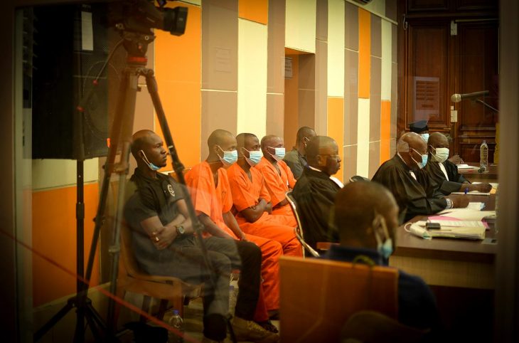 3 prisonniers en combinaisons orange sont assis dans un tribunal (Cour pénale spéciale en Centrafrique). Magistrats, policiers, caméra vidéo.