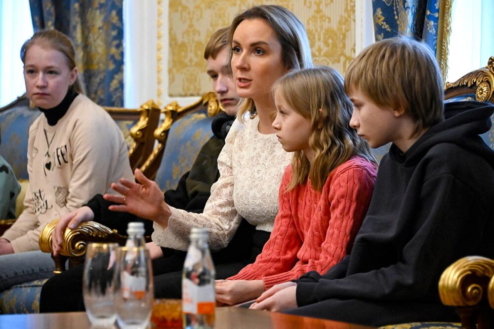 Vladimir Poutine et Maria Lvova-Belova sont accusés de déportation (d'enfants ukrainiens) en tant que crime de guerre par la Cour pénale internationale (CPI). Photo : Belova et 4 enfants sont assis dans un salon.