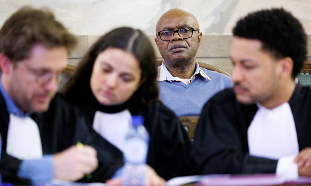 Trial in Belgium of Emmanuel Nkunduwimye, accused of genocide in Rwanda. Photo: Nkunduwimye stares into the camera behind his discussing lawyers.