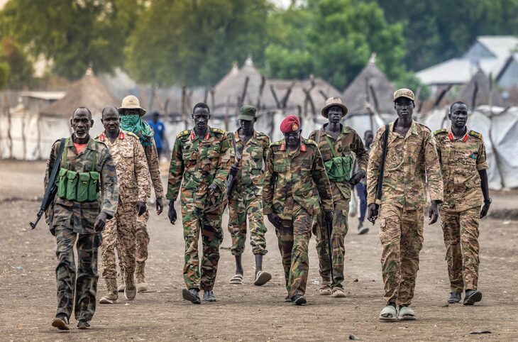Au Sud-Soudan, une guerre civile s'apprête à embraser le pays alors que les processus de justice transitionnelle patinent. Photo : un groupe de soldats en uniformes dépareillés (seuls quelques-uns sont armés) de l'Armée populaire de libération du Soudan marche avec des chaussures inadaptées.