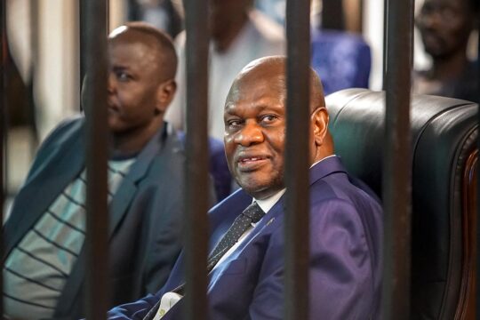 Trial of former Vice President Riek Machar in South Sudan. Photo: Machar, seated in a comfortable chair, smiles at the photographer from behind bars.