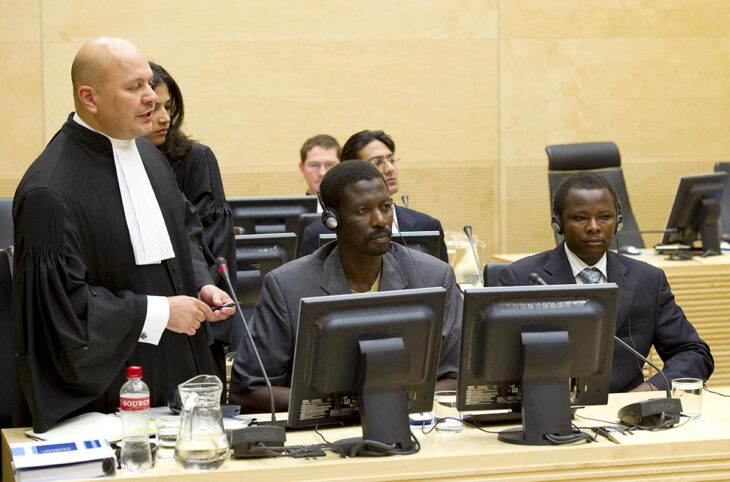 Devant la Cour pénale internationale (CPI), deux personnes accusées de crimes de guerre au Darfour (Soudan), Abdallah Banda Abakaer Nourain et Saleh Mohammed Jerbo Jamus, sont assises à côté de Karim Khan (ex-avocat de la défense devenu procureur de la CPI) qui se tient debout en habits de magistrat.