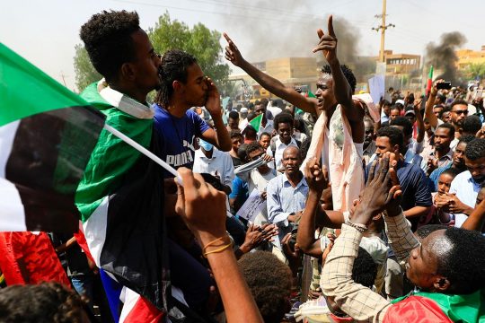 Sudanese protesters march in Khartoum, waving flags of Sudan