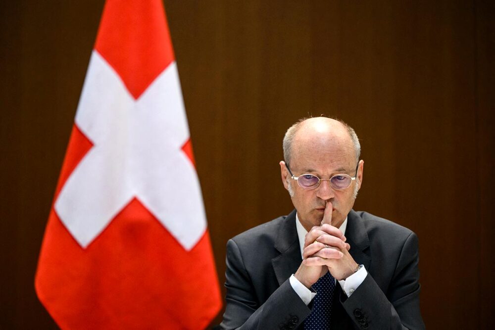 La justice internationale suisse (sous le principe de la compétence universelle) s'enlise dans des lenteurs et des suspicions d'ingérences politiques. Photo : Stefan Blattler, procureur général, en pleine réflexion, à côté d'un drapeau suisse.