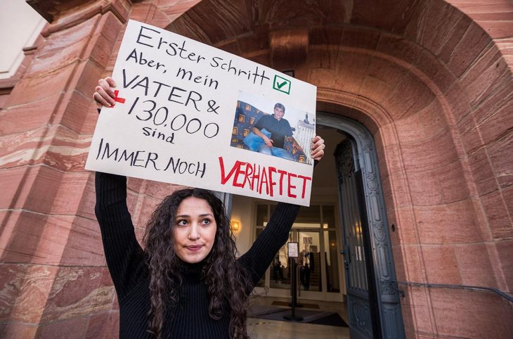 Sedra Alshehabi stands with a placard with the picture of her father Ali and a text reading 'First step but my father and 130000 are still in jail' after the verdict in the trail of Syrian defendant Eyad al-Gharib