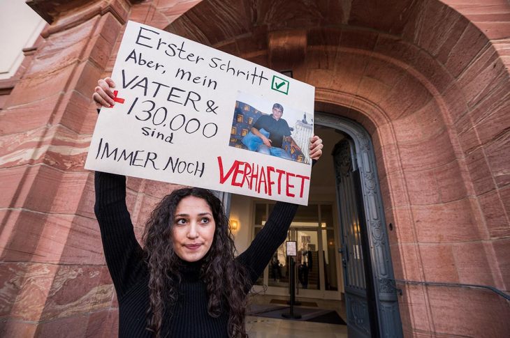 Sedra Alshehabi stands with a placard with the picture of her father Ali and a text reading 'First step but my father and 130000 are still in jail' after the verdict in the trail of Syrian defendant Eyad al-Gharib