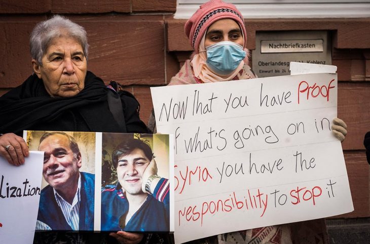 2 Syrian victims and activists demonstrate with signs outside the court in Koblenz, Germany, following the trial of Anwar Raslan