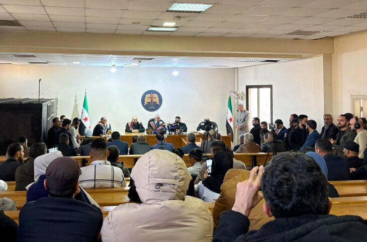 Un tribunal syrien basé à Alep juge, en public, les auteurs présumés de crimes commis en mars 2025 en Syrie. Photo : une salle d'audience comble, entourée de journalistes avec une cage en fer sur le côté.