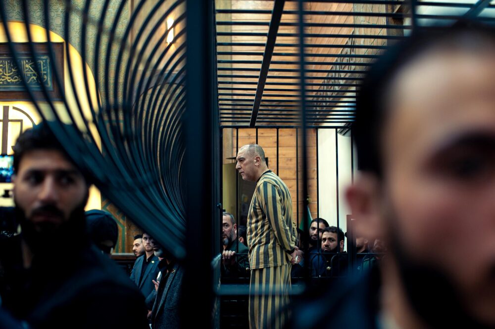 Premier procès de justice transitionnelle en Syrie. Photo : Atef Najib (ancien haut dignitaire du régime de Bachar al-Assad), en habits rayés de prisonnier et crâne rasé, se tient debout dans son box, derrière des barreaux.