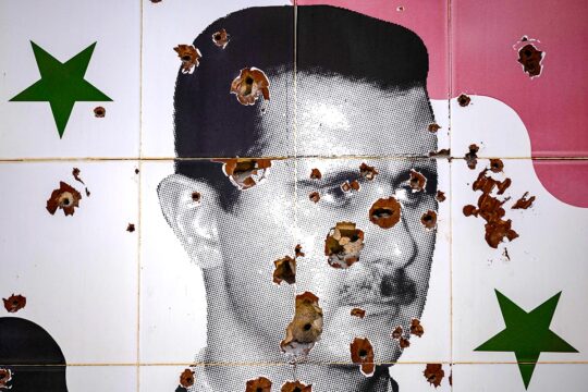 Portrait de Bachar el-Assad peint sur un mur en Syrie, comportant des impacts de balles.