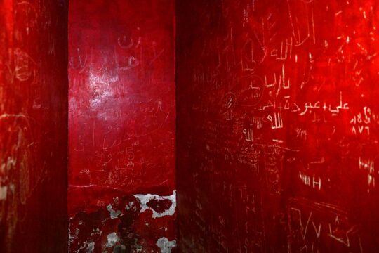 In Syria, under Bashar al-Assad’s regime, torture was rife in Branch 251 prison (or Al-Khatib). Today, Syrians are seeking justice for these crimes. Photo: a very cramped cell, painted entirely red and covered in Arabic inscriptions.