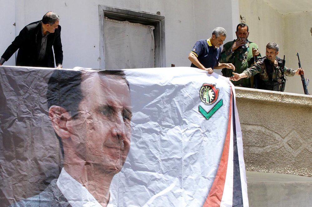 En Syrie, les Forces de défense nationale (NDF) sont une milice accusée d'avoir perpétré des crimes tels que torture, violences sexuelles et disparitions forcées. Photo : des membres des NDF accrochent un portrait de Bachar al-Assad sur le mur d'un bâtiment.