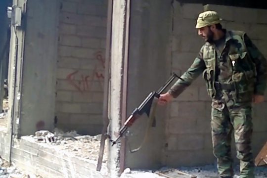 A soldier of the Syrian government army points his weapon at a large hole whose bottom is not visible