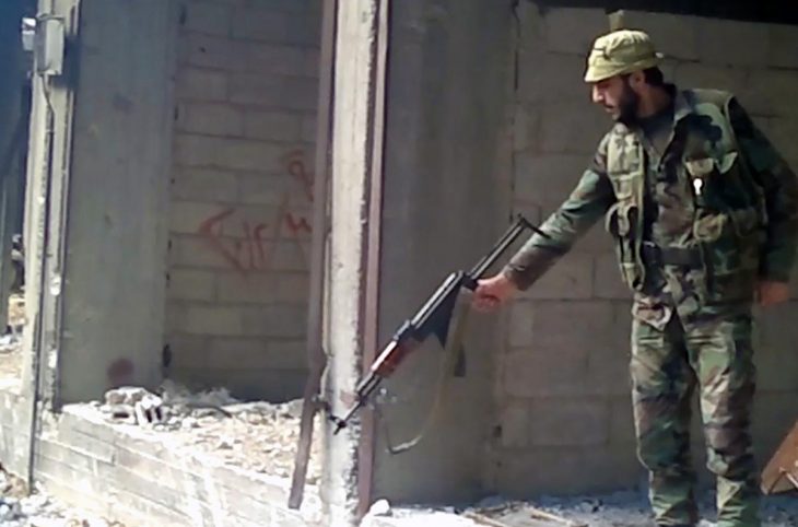 A soldier of the Syrian government army points his weapon at a large hole whose bottom is not visible