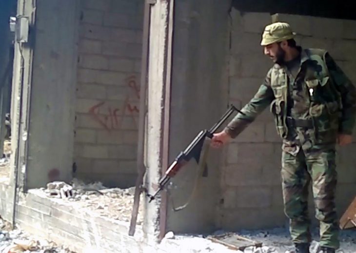 A soldier of the Syrian government army points his weapon at a large hole whose bottom is not visible