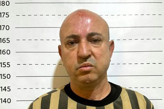 Wassim Al-Assad was arrested in Syria. Photo: Al-Assad poses in front of a measuring ladder, wearing a prison uniform (yellow and black stripes).