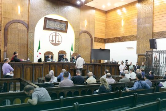 En Syrie, des personnes sont jugées pour leur participation aux crimes commis sous le régime de Bachar al-Assad. Photo : Procès de Wasim al-Assad, debout dans une cage sur le côté d'une salle d'audience relativement vide.