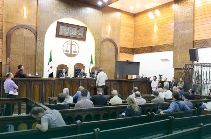 En Syrie, des personnes sont jugées pour leur participation aux crimes commis sous le régime de Bachar al-Assad. Photo : Procès de Wasim al-Assad, debout dans une cage sur le côté d'une salle d'audience relativement vide.