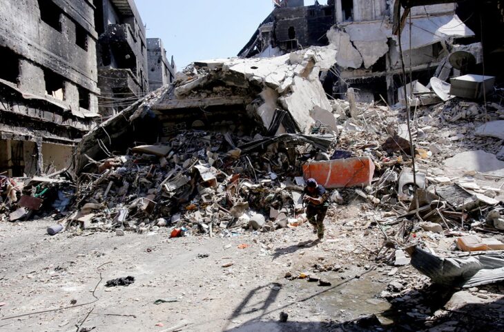 En Syrie, un combattant armé du Front populaire de libération de la Palestine, allié au président syrien Bachar el-Assad, traverse une rue dans le camp de réfugiés de Yarmouk.