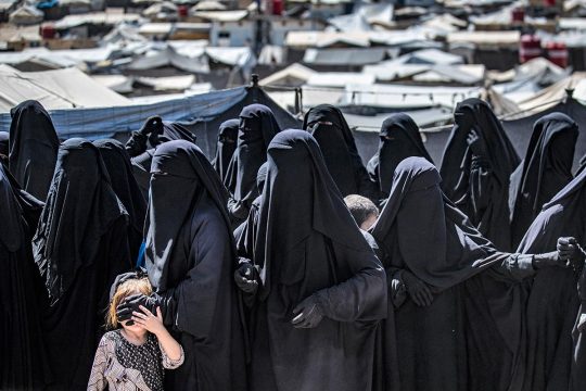 Des femmes vêtues intégralement de noir et un enfant font la queue dans un camp de réfugiés