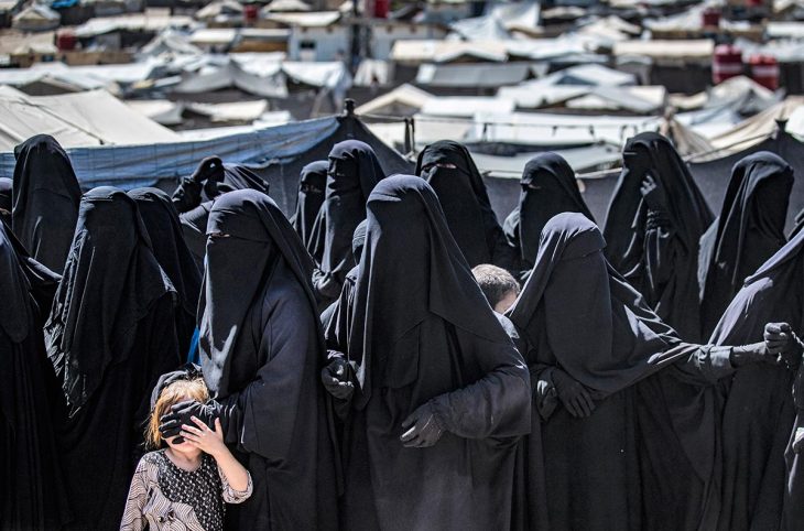 Des femmes vêtues intégralement de noir et un enfant font la queue dans un camp de réfugiés