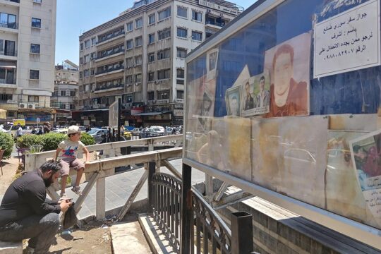 Disparitions forcées en Syrie, une commission est créée - Photo : un homme et un enfant devant un panneau affichant les portraits de personnes disparues.