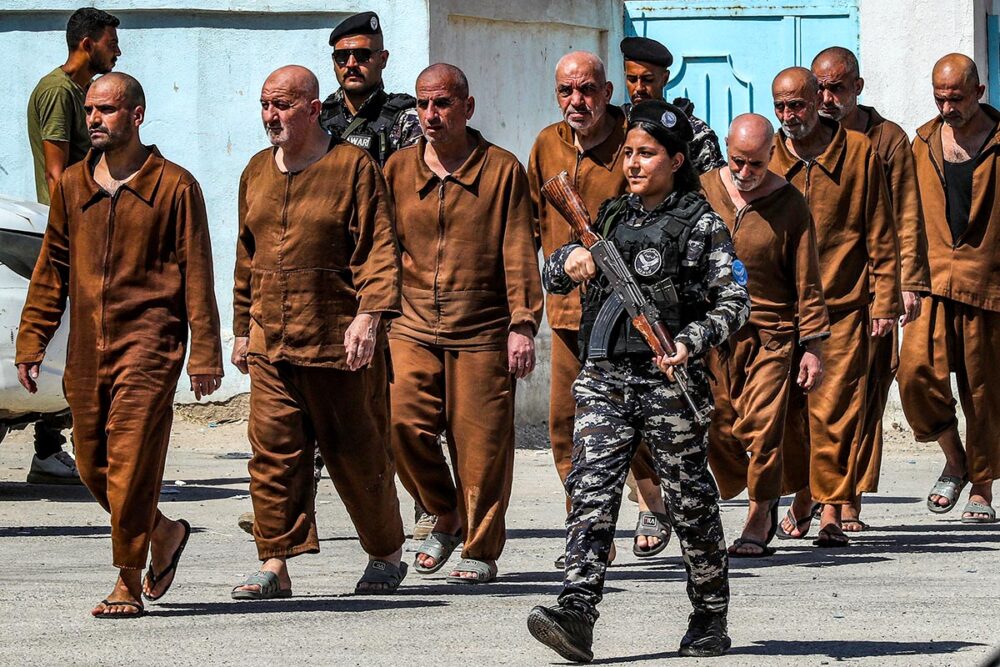 Des milliers de prisonniers suspectés de faire partie de l'Etat Islamique (Daech) ont été transférés de la Syrie vers l'Irak. Photo : un groupe de prisonniers en uniformes oranges sales sort d'une prison escorté par un soldat armé.