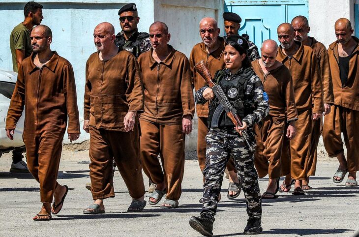 Des milliers de prisonniers suspectés de faire partie de l'Etat Islamique (Daech) ont été transférés de la Syrie vers l'Irak. Photo : un groupe de prisonniers en uniformes oranges sales sort d'une prison escorté par un soldat armé.