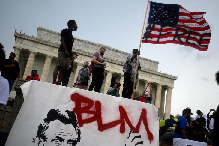 A man holds an American flag with the words 'Not free' on it, in front of the Lincoln Memorial in Washington (USA)
