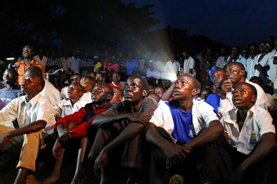 Joseph Kony was the leader of a Ugandan rebel group, the Lord's Resistance Army (LRA), which was tried before the ICC in The Hague for war crimes. Photo: Ugandans gather in a village to watch a film about Kony. Sitting on the ground, they seem fascinated by the images they see.