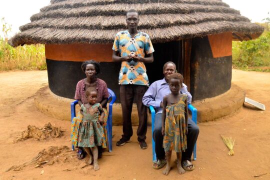 Reportage dans le village de naissance de Thomas Kwoyelo, en Ouganda, auprès de sa famille. Photo : des proches de Kwoyelo devant la maison où il a vécu enfant.