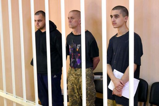 3 soldiers (Aiden Aslin, Shaun Pinner and Brahim Saadoun) stand behind bars