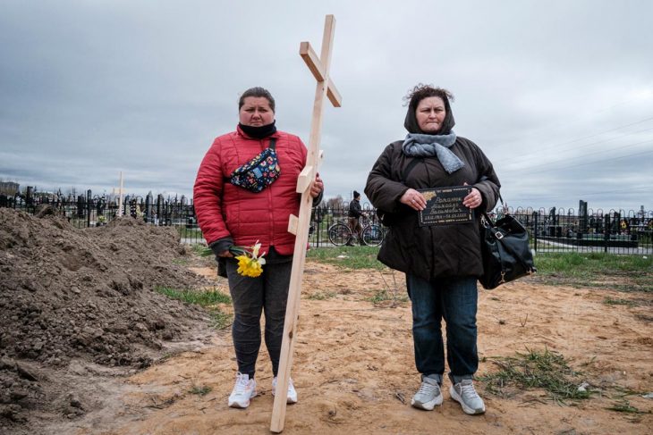 Two women (one holding a cross) in a cemetery in Bucha, Ukraine.