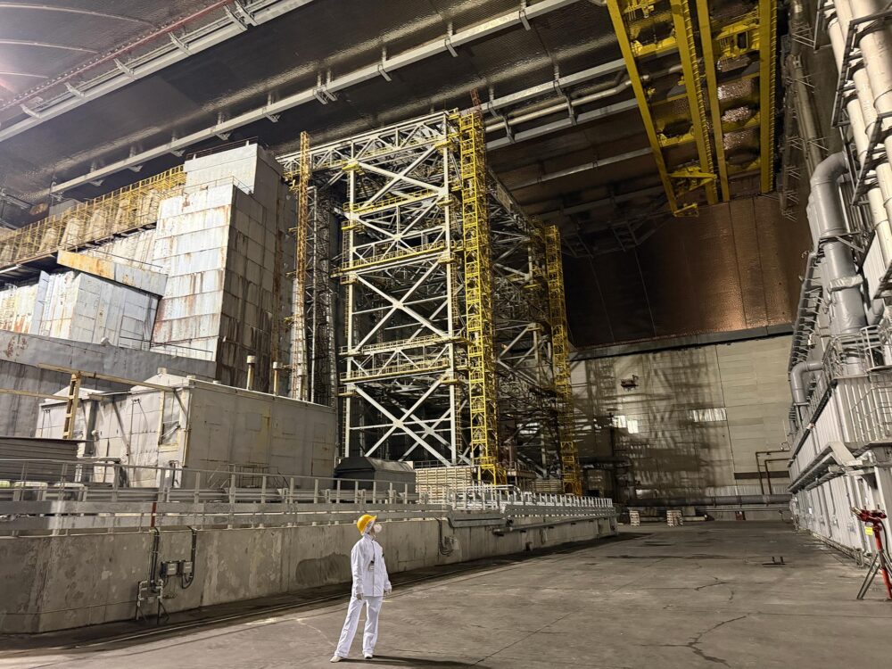 En Ukraine, la centrale nucléaire de Tchernobyl a été attaquée et endommagée par une attaque de drone russe. État des lieux et focus sur le droit international en pareilles circonstances. Photo : notre correspondante en Ukraine pose, en habits de sécurité, sous l'arche de béton.