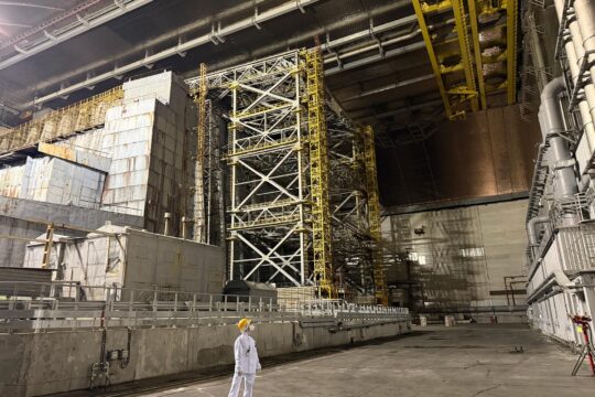 En Ukraine, la centrale nucléaire de Tchernobyl a été attaquée et endommagée par une attaque de drone russe. État des lieux et focus sur le droit international en pareilles circonstances. Photo : notre correspondante en Ukraine pose, en habits de sécurité, sous l'arche de béton.
