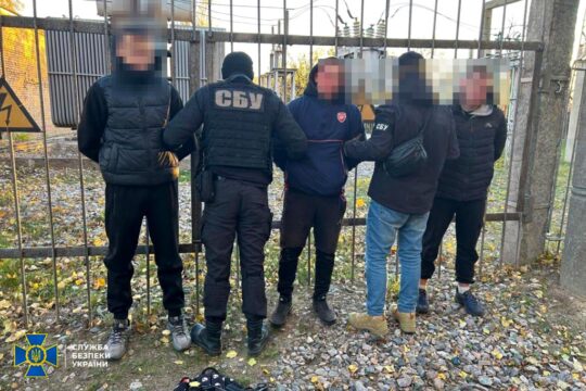 Des adolescents recrutés par le FSB russe sont arrêtés en Ukraine. Photo : 3 adolescents (visages floutés, mains dans le dos) sont arrêtés par 2 policiers ukrainiens, devant une grille.