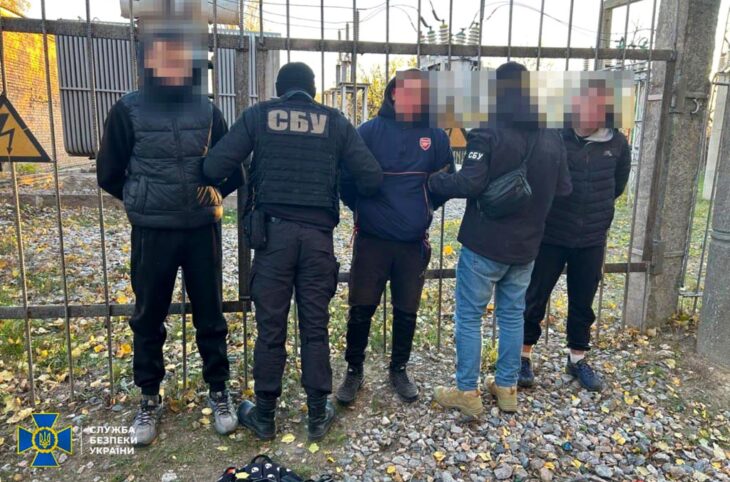 Teenagers recruited by the Russian FSB are arrested in Ukraine. Photo: 3 teenagers (faces blurred, hands behind their backs) are arrested by 2 Ukrainian police officers in front of a gate.