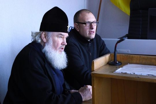 Le prêtre orthodoxe ukrainien Joasaph et son avocat sont assis côte à côte lors d'un procès en Ukraine.