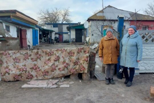Procès in absentia en Ukraine. Photo : deux femmes se tiennent devant une habitation détruite dans le village de Lukashivka en Ukraine.