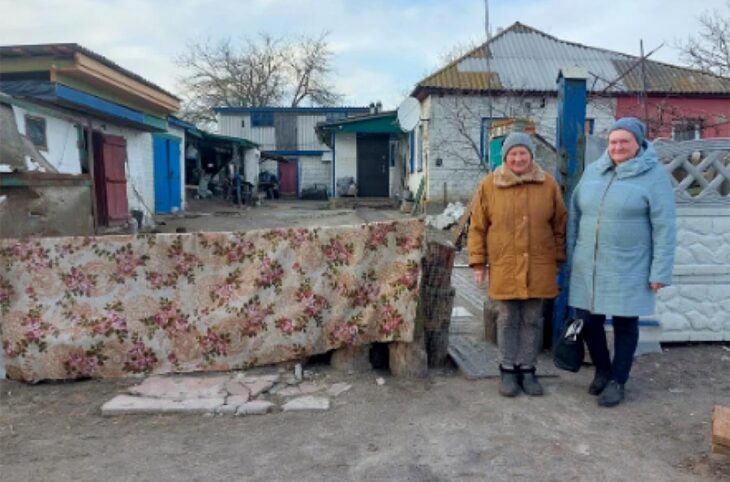Procès in absentia en Ukraine. Photo : deux femmes se tiennent devant une habitation détruite dans le village de Lukashivka en Ukraine.