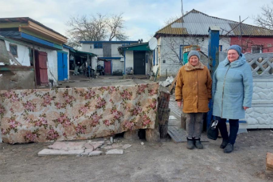 Procès in absentia en Ukraine. Photo : deux femmes se tiennent devant une habitation détruite dans le village de Lukashivka en Ukraine.