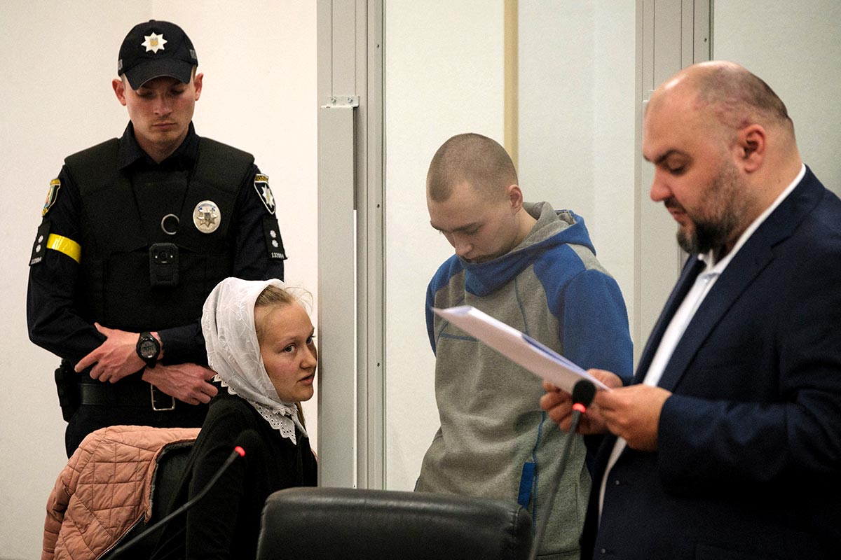 Ukrainian defense lawyer Viktor Ovsyannikov reads his notes while a translator talks to Shishimarin, head down.