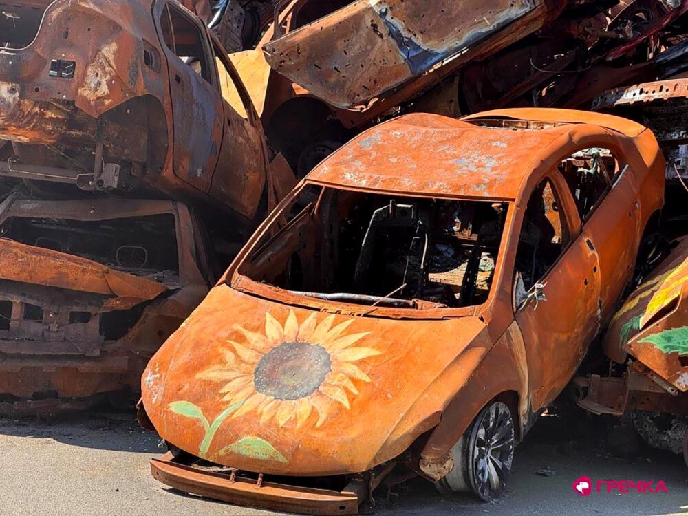 En mémoire des victimes de la guerre à Irpin (Ukraine), des monuments et des projets artistiques sont mis en place. Photo : des épaves de voitures calcinées et jaunies sont entassées. Des tournesols sont peints dessus.